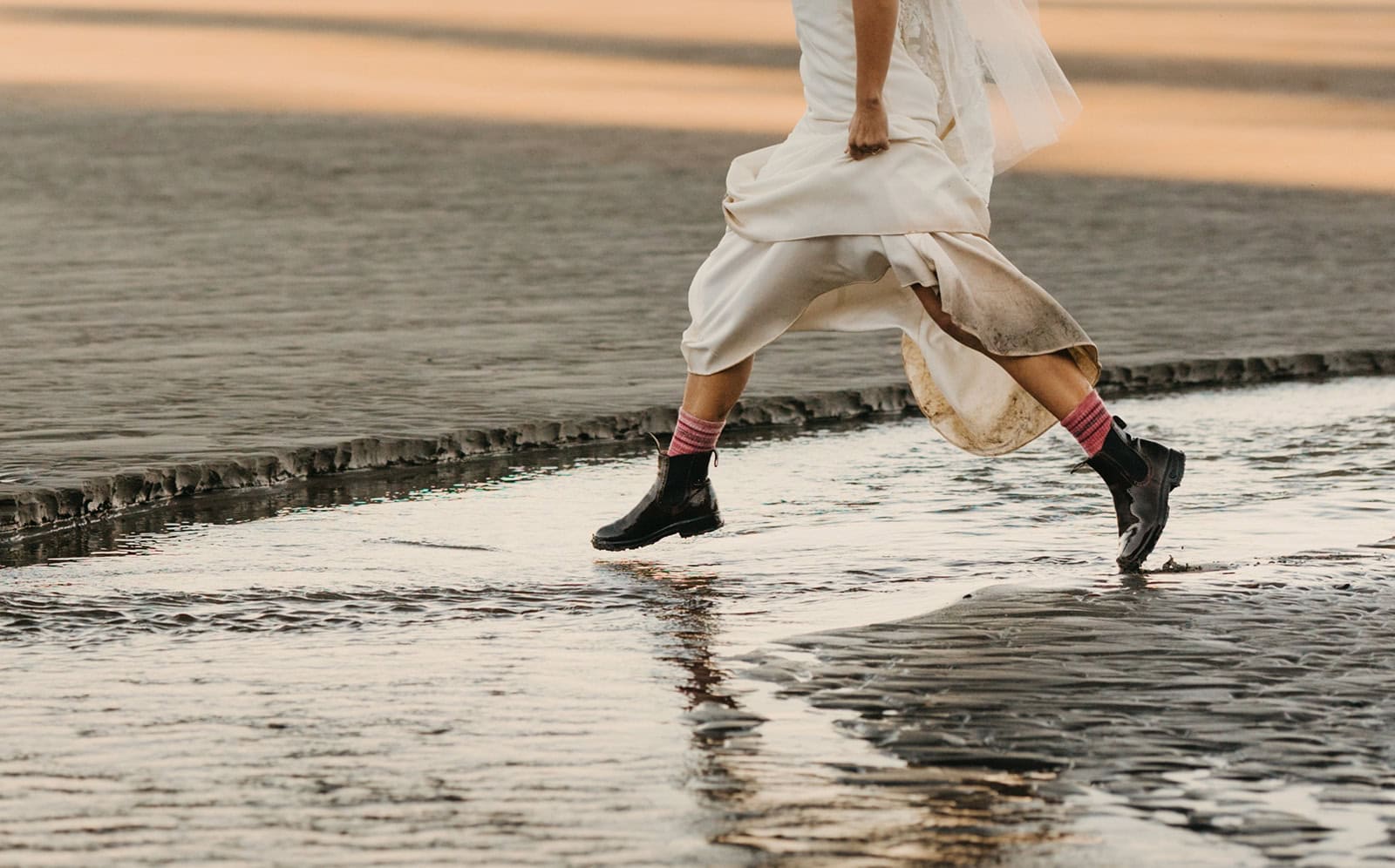 A bride jumps across a river in her Blundstones.
