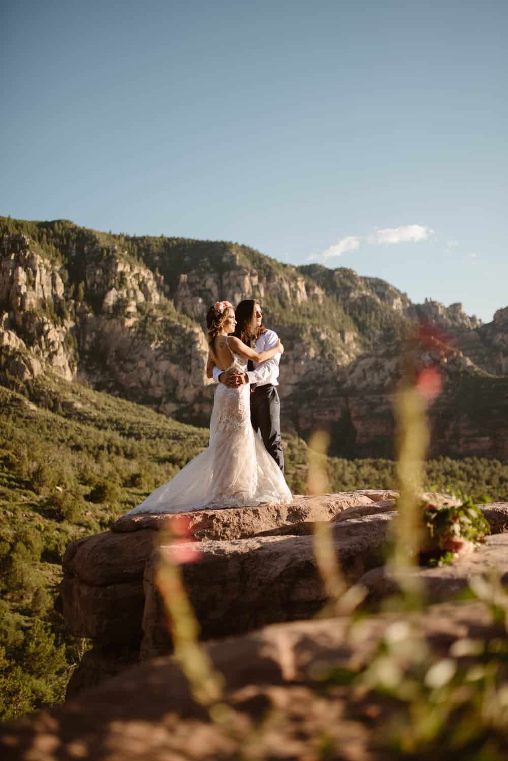A groom holds his bride close as they look at the sunset together.