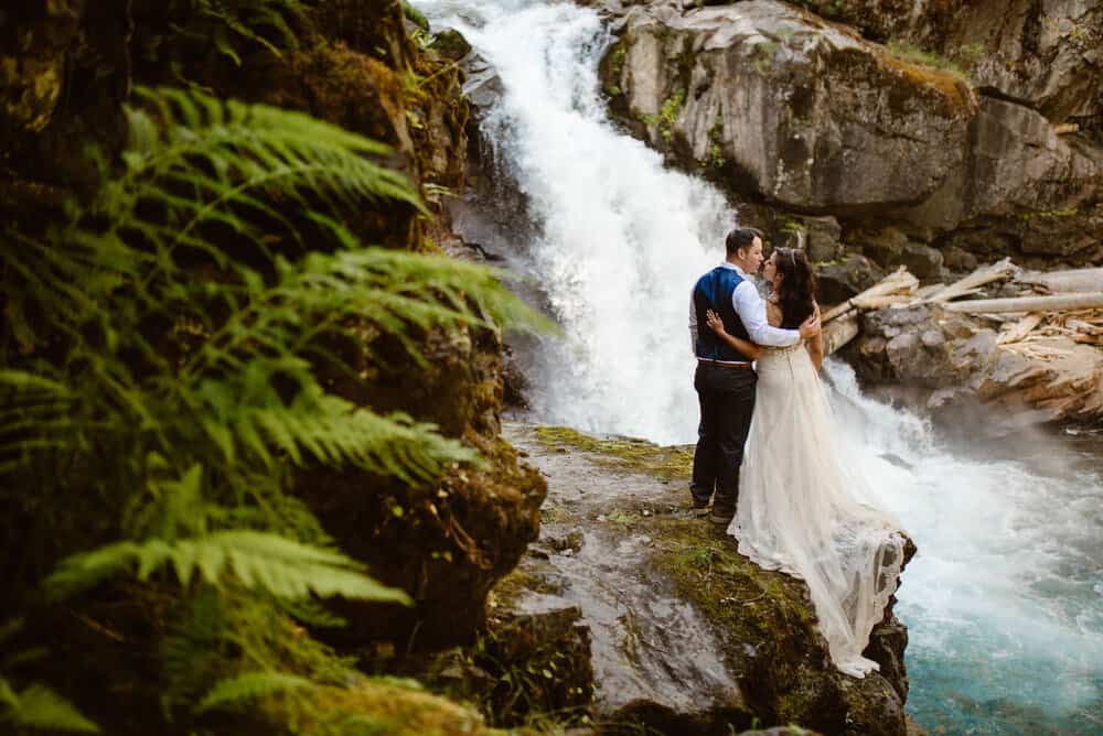 A couple shares a kiss while admiring a waterfall.