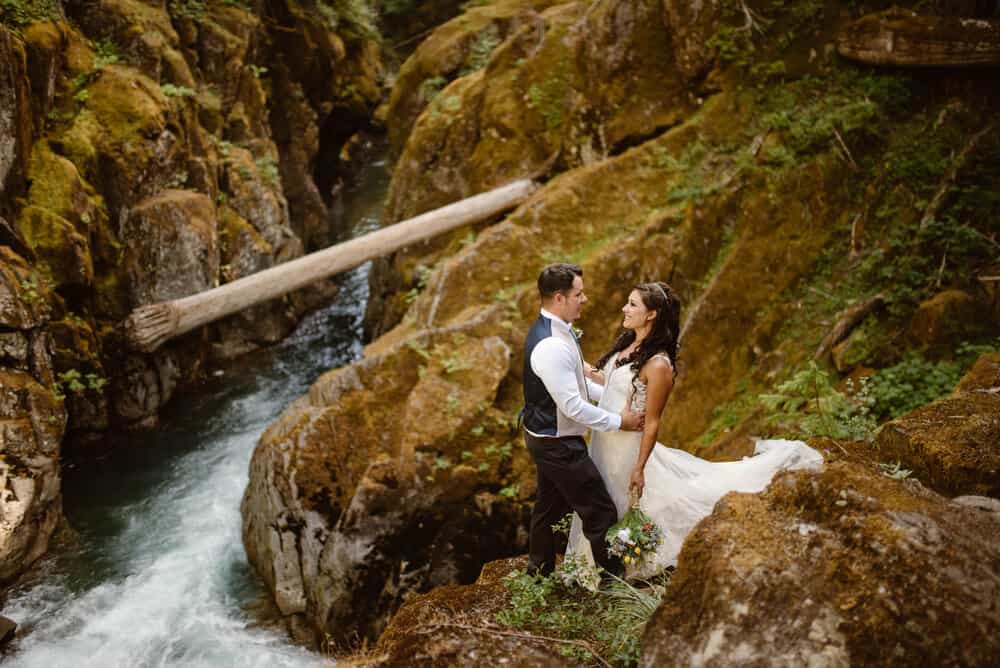 A couple stands together surrounded by mossy rock.
