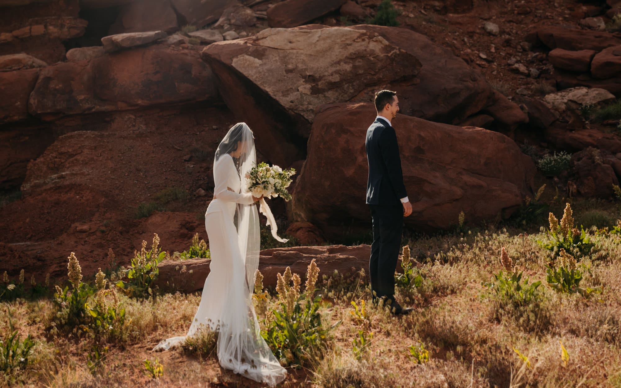 A brides veil blocks her face as she walks towards her groom for the first look.