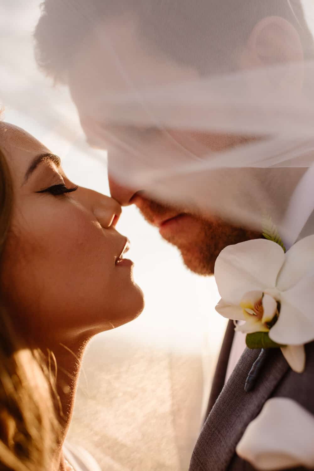A bride and groom stand close together for a detail photograph under the veil.