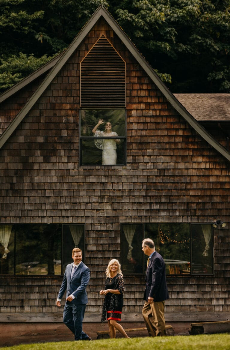 A bride waves out of a cabin window before their elopement ceremony.