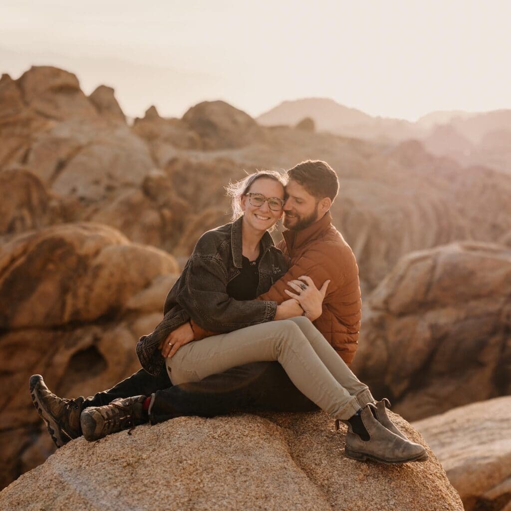 A man and woman sit together among the white granite of Joshua Tree at sunset.