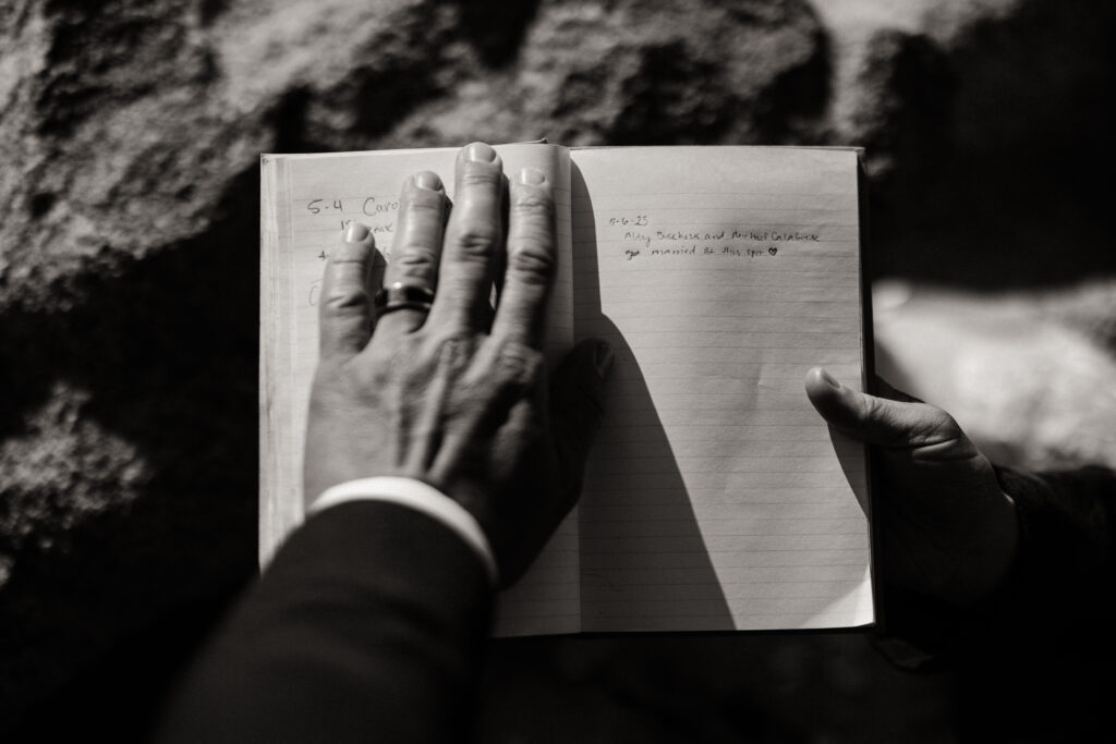 The couples hands as their write in the summit registery on the trail.