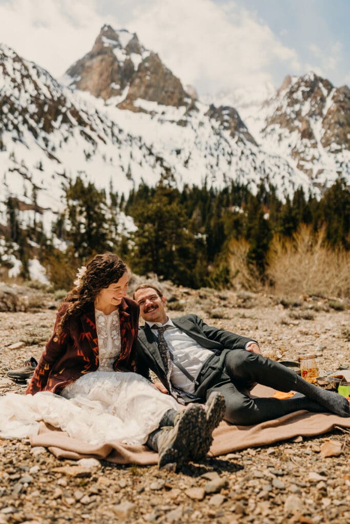 The couple sits together and laughs while chatting at their picnic.