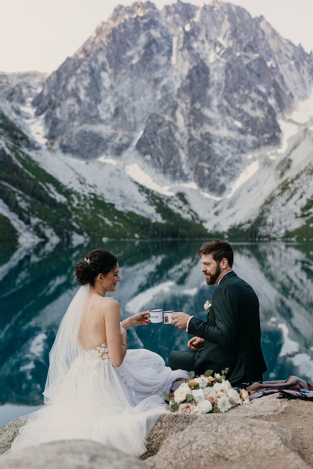 A bride and groom sit together at Colchuck Lake.