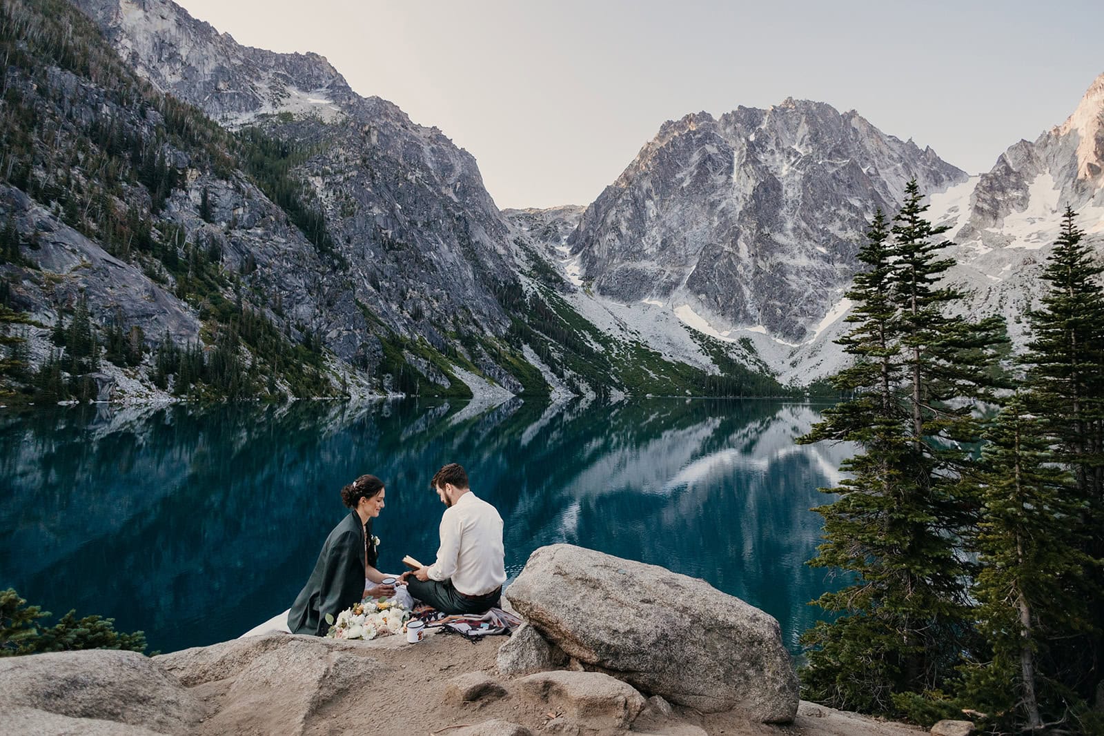 A bride and groom sit together at Colchuck Lake.