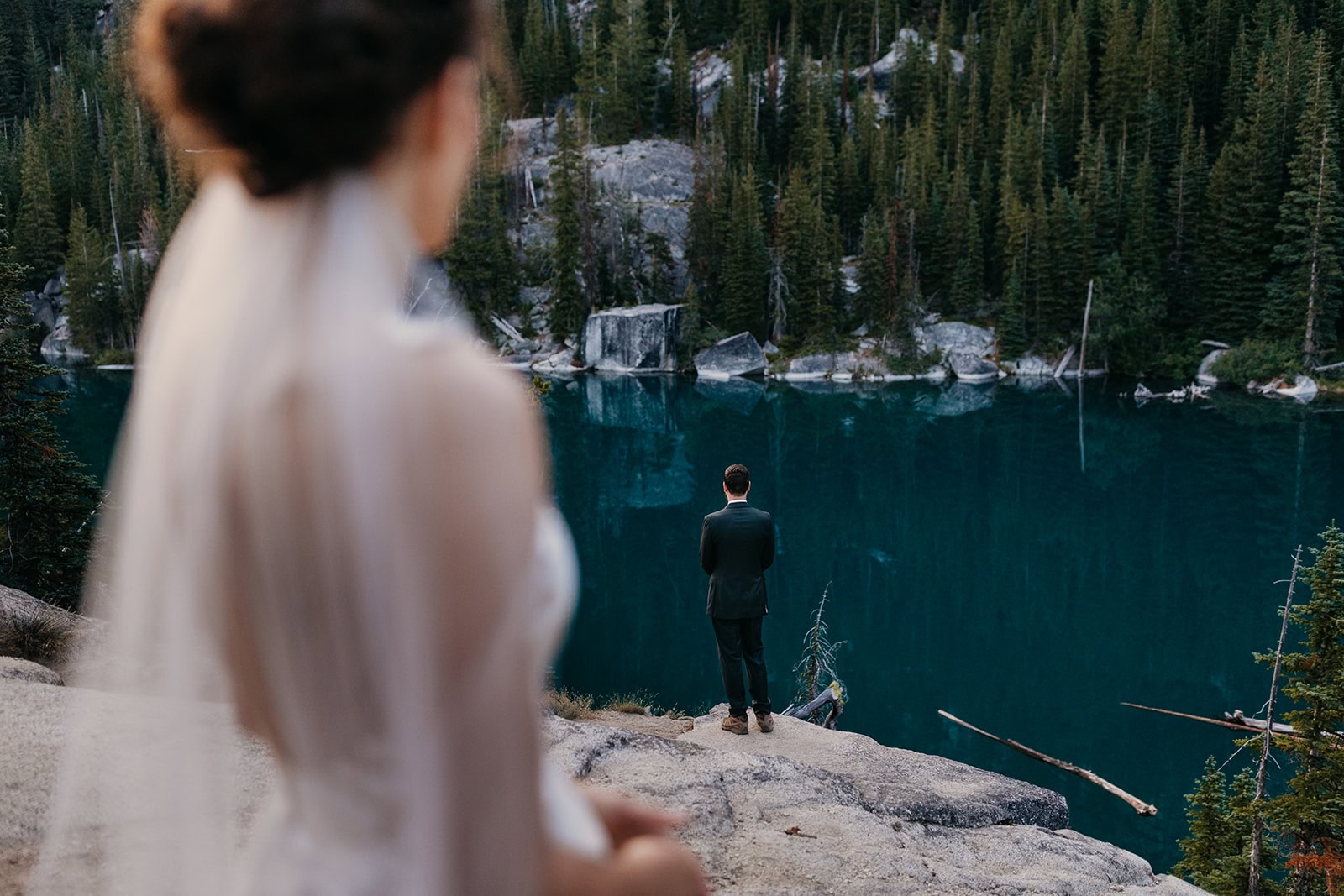 An image captured over a brides shoulder looking towards the groom while at Colchuck Lake