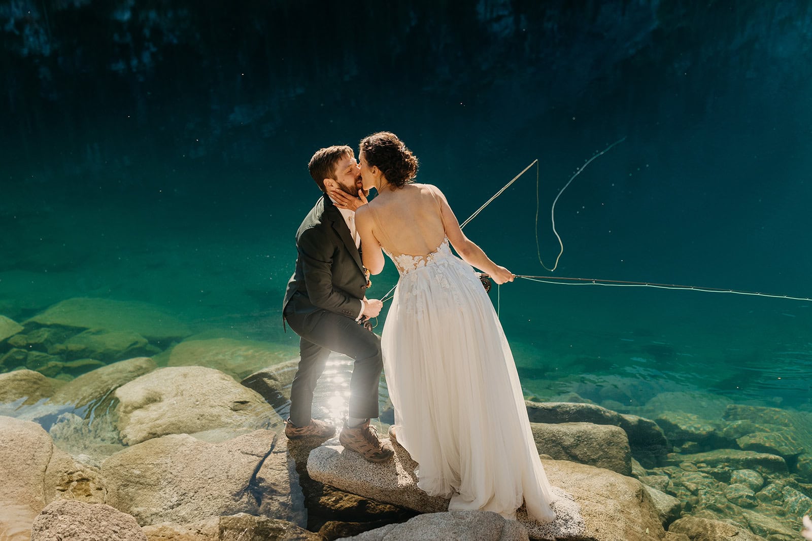 A view of the back of a bride's wedding dress as she kisses her groom fishing.