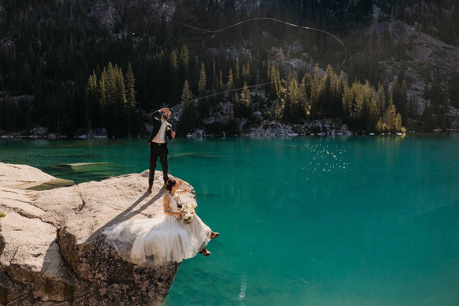 A couple fly fishes on their elopement day at an alpine lake.