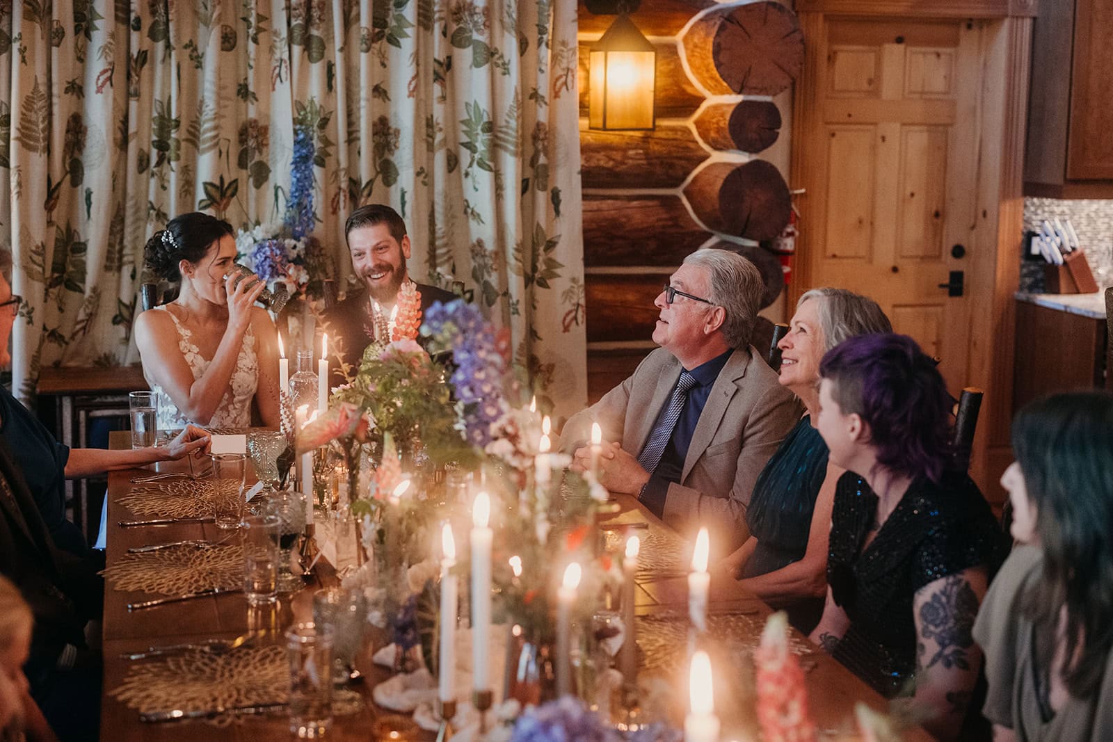 A family sits at a table with lit candlesticks enjoying a dinner while laughing.