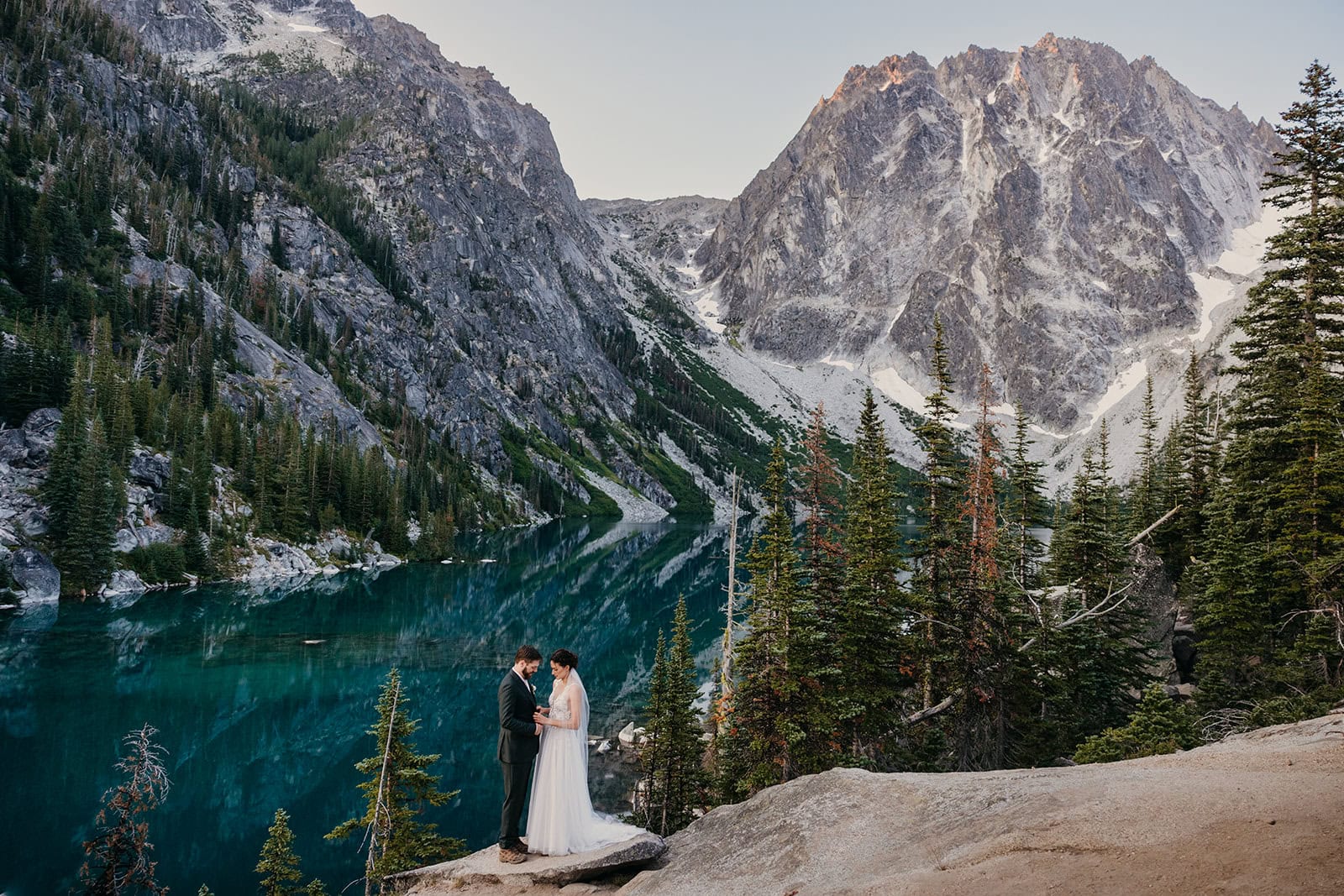 A bride and groom stand together at Colchuck Lake.