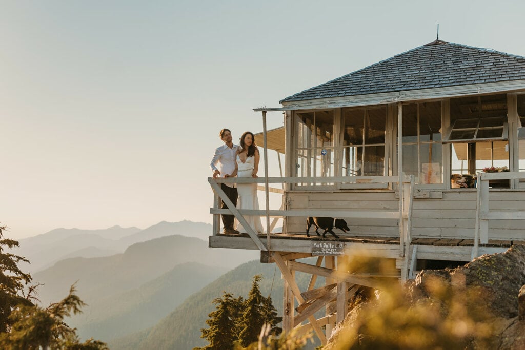 A couple stands on the deck of a fire tower watching sunset.
