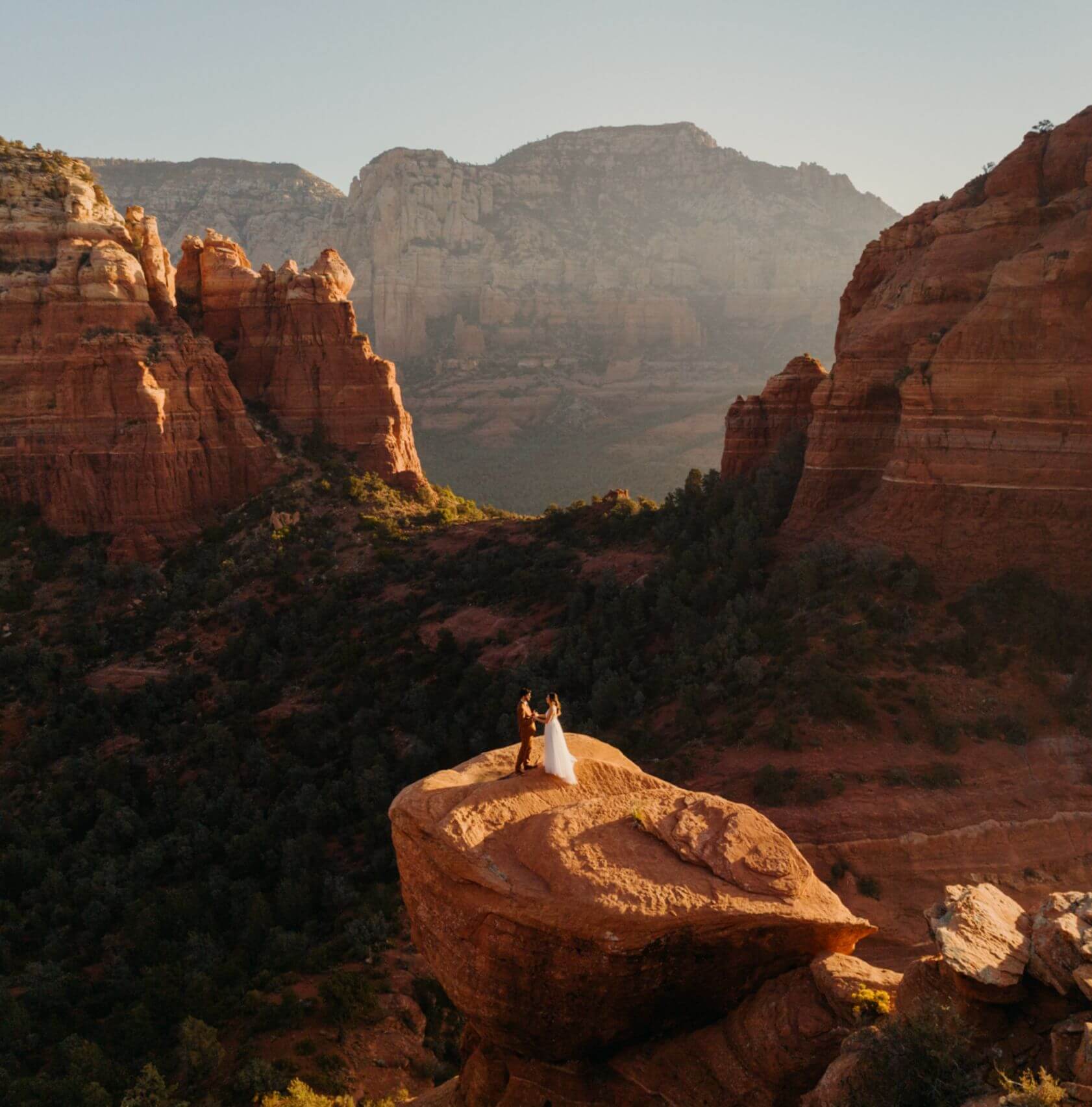 Aerial view of a newlywed couple standing on a rock overlooking a canyon