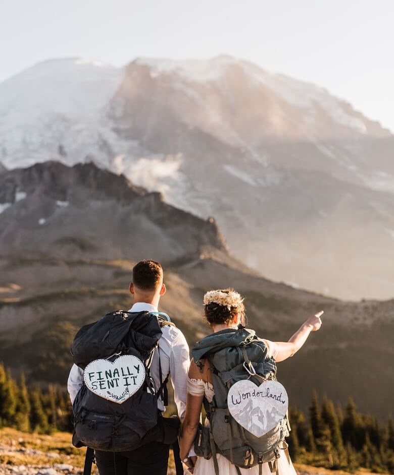 A newlywed couple with hiking backpacks on pointing off to into the distance 