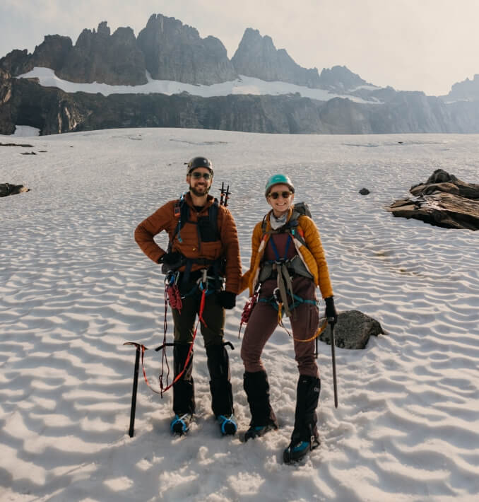 Two people smiling while wearing hiking gear and standing in the snow 