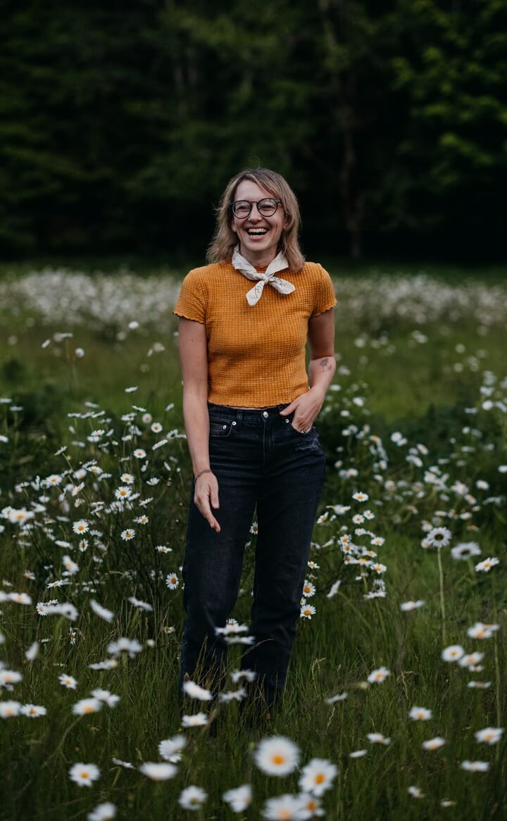 A person standing in a field of tall grass and while flowers smiling 
