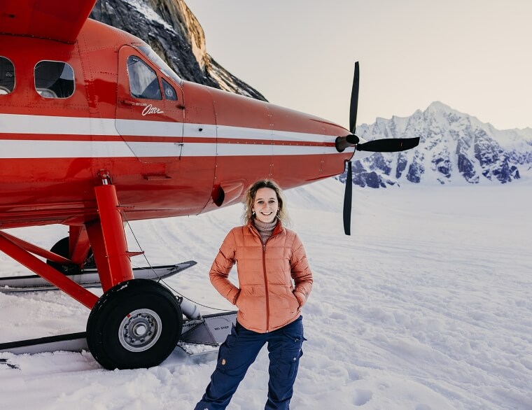 A person standing in front of a small plane on a snowy runway 