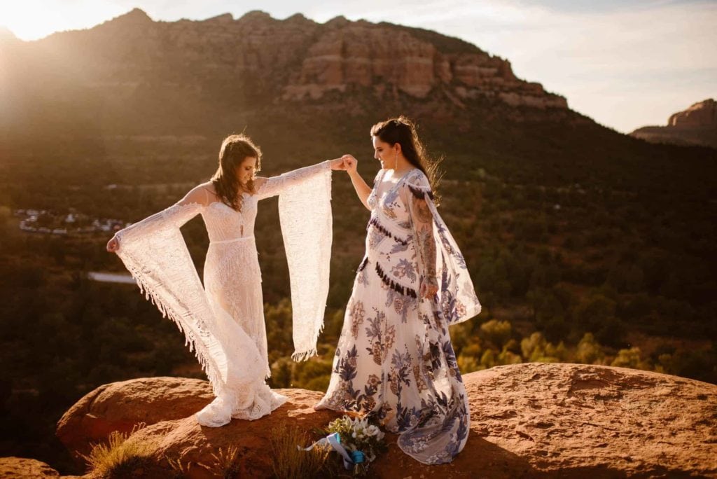 Two brides dance in the sunlight in their dresses.