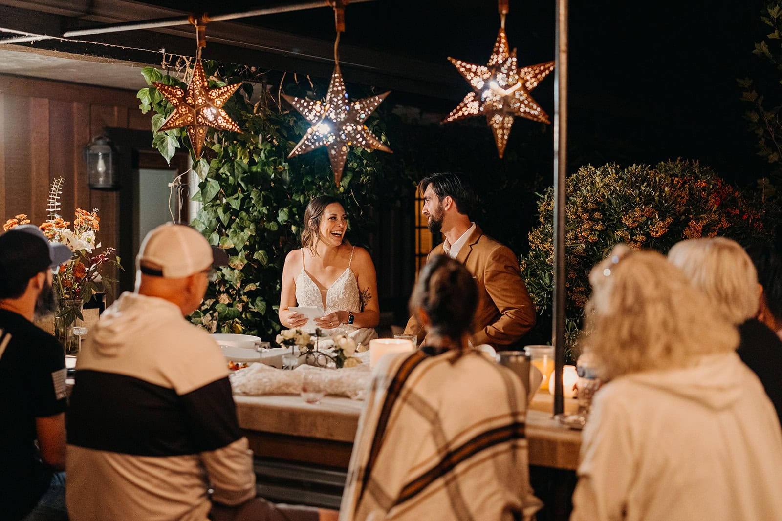 A couple chat with their dinner celebration guest under twinkle lights.