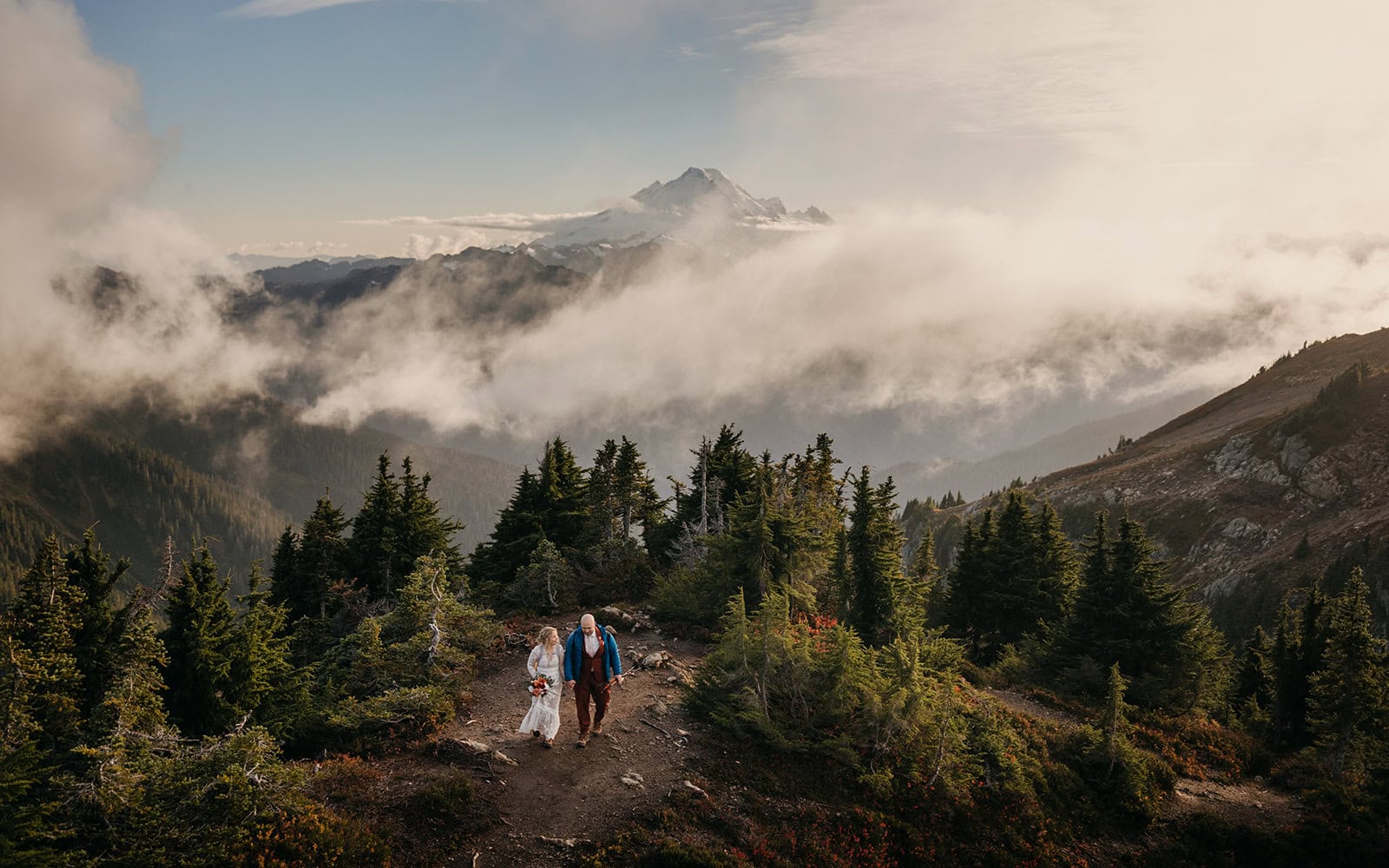 A couple hikes up a mountain trail together to their elopement ceremony.