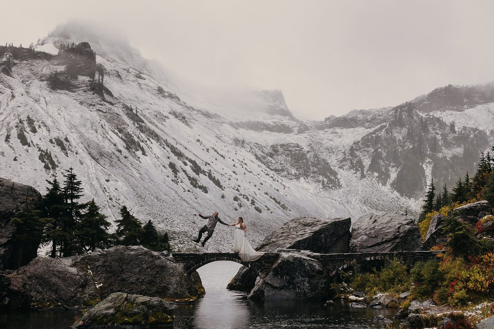A groom jumps for joy in the mountains on a snowy day. 
