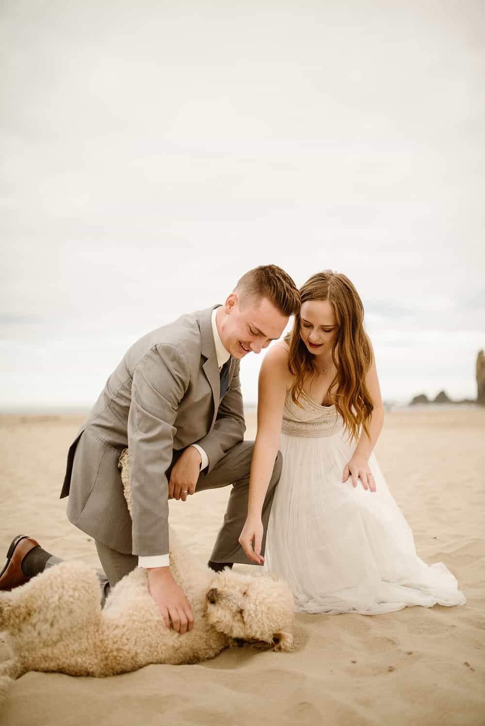 A couple pets their dog as it rolls around on the beach.