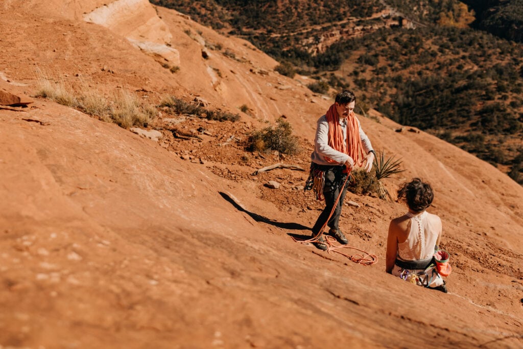 A bride and groom preparing to continue their climb as the groom flakes the rope over his shoulders