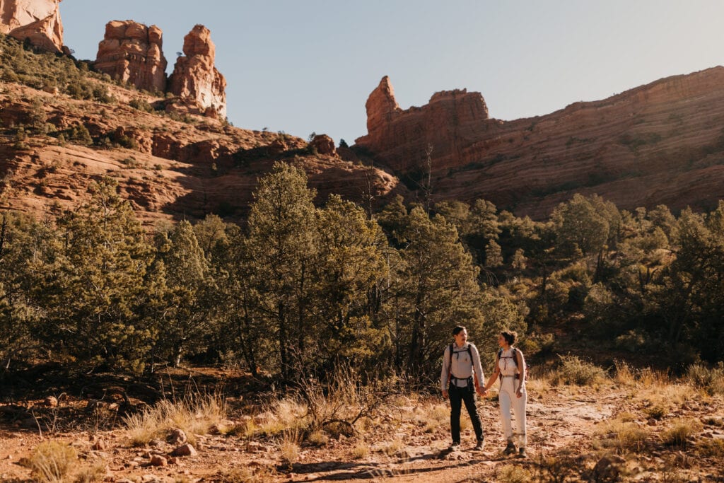 A couple hikes out to where they will be climbing together holding hands on the trail.