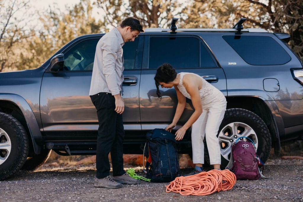 A couple prepares for a rock climbing adventure by their car.