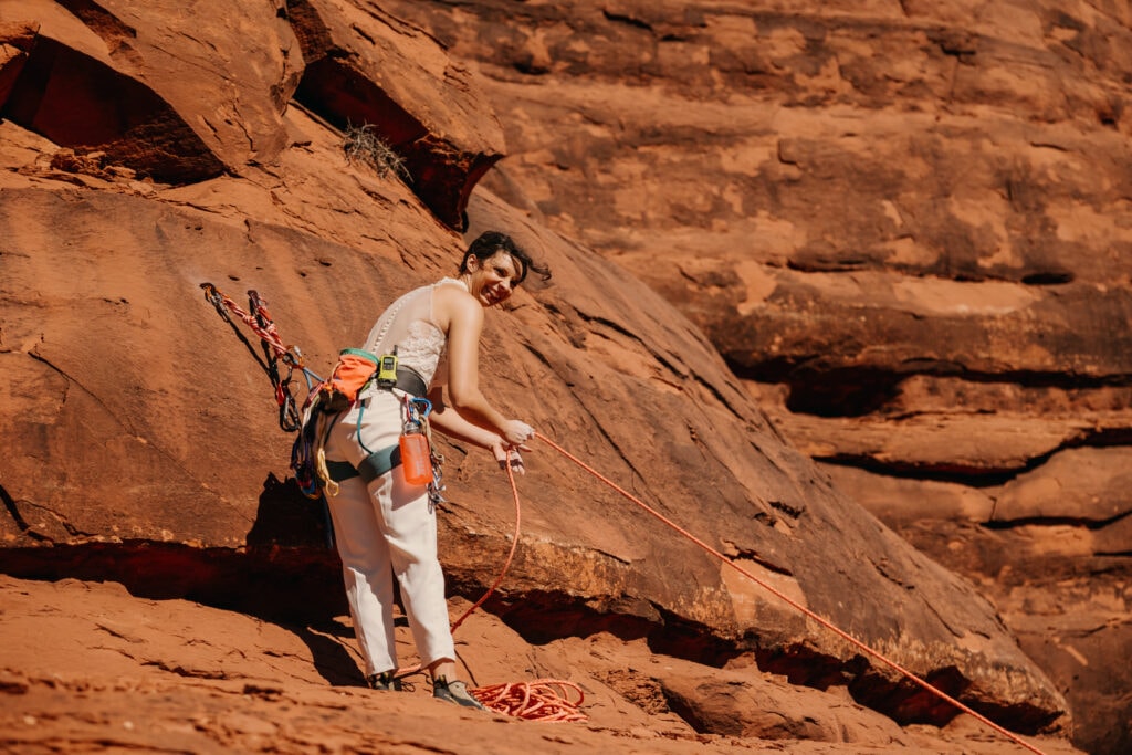 A bride looks back as she finishes building an anchor while climbing in Sedona