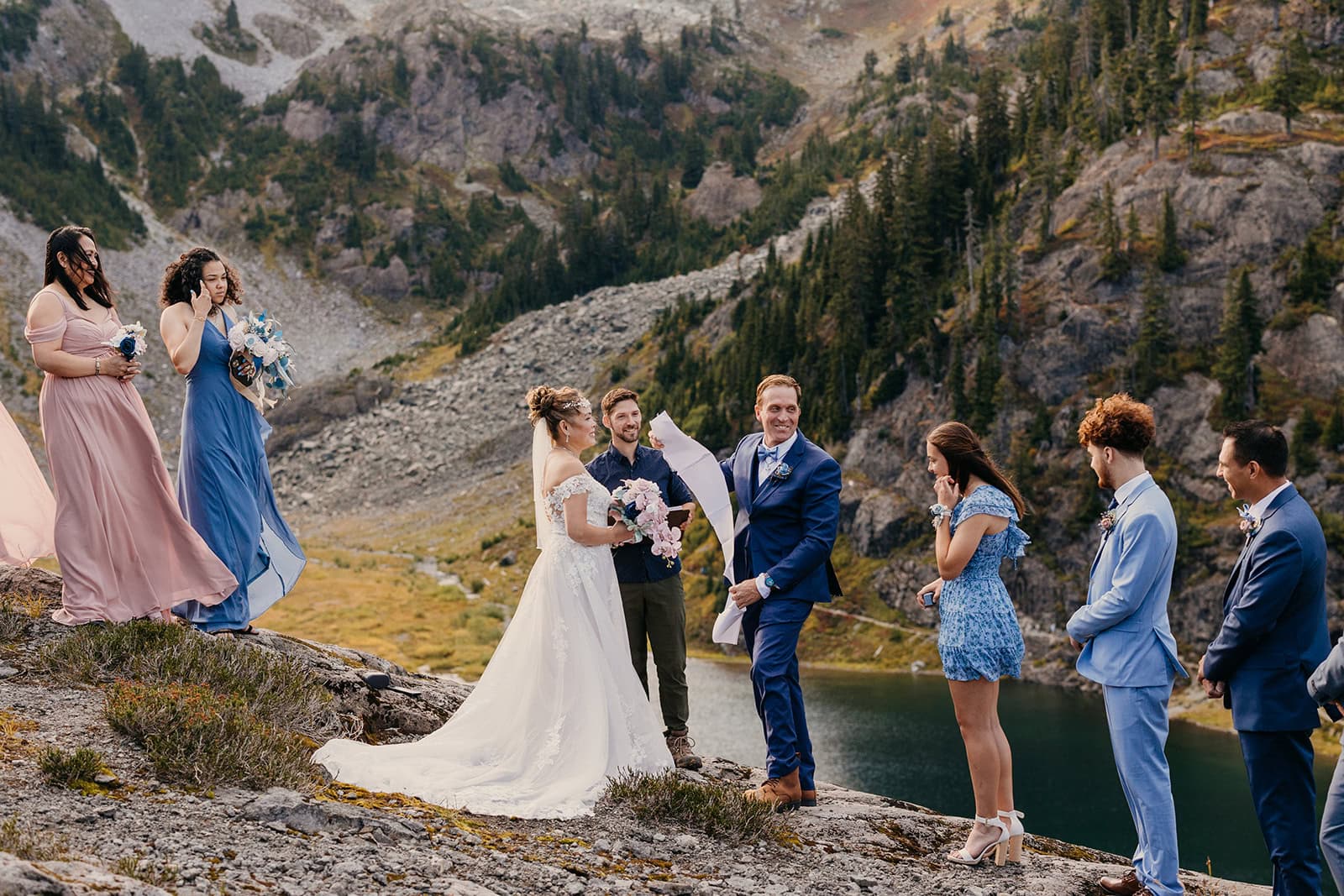 A groom pulls his long vows out of his jacket pocket as their guests react at heather meadows.