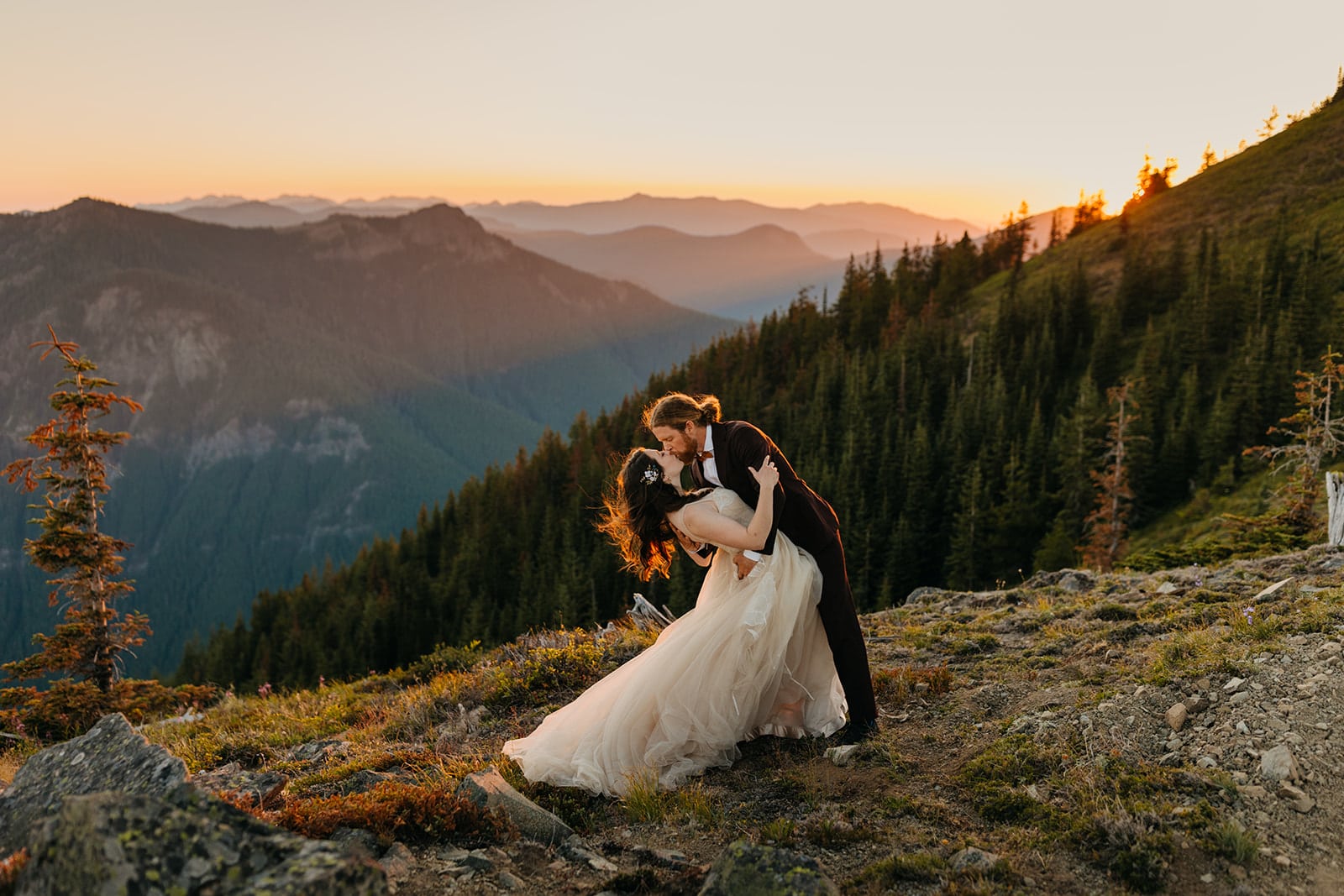 A couple shares a passionate kiss in the mountains at sunset.