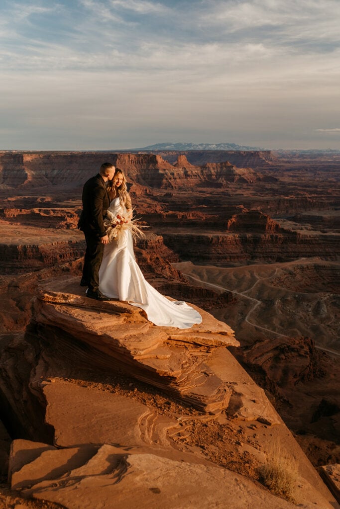 A bride and groom stand together at Dead Horse Point at Sunset