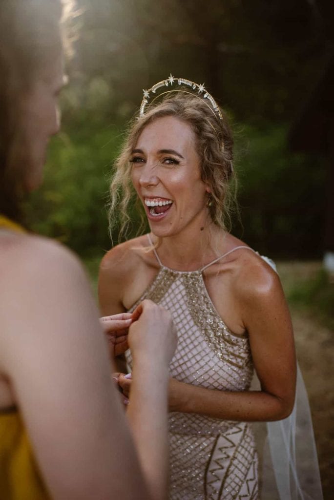 The bride laughs as she puts her ear rings in.
