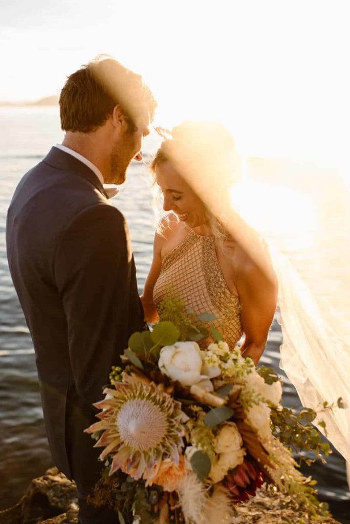 a bride and groom smiling. the bride is looking down, holding her bouquet.