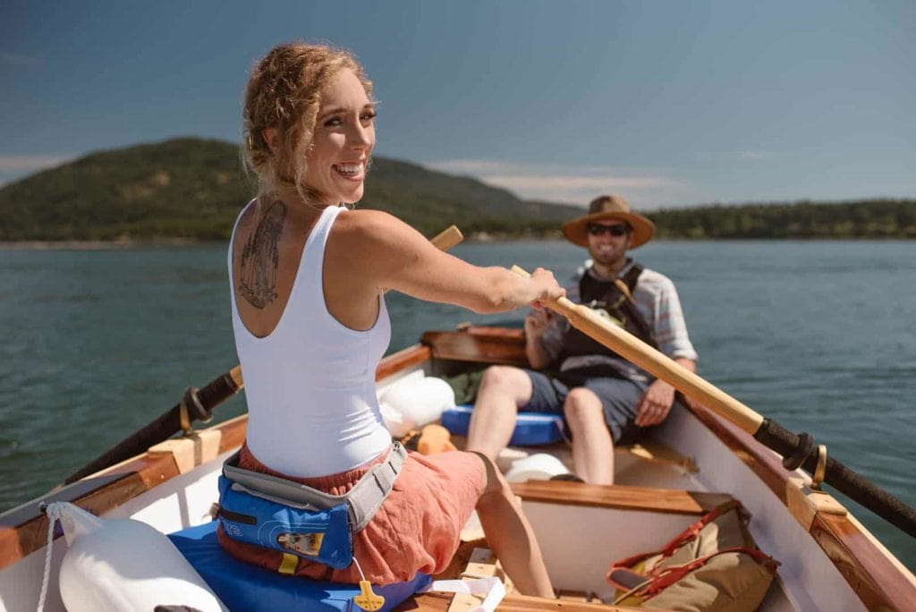 A bride smiles at the camera while rowing a boat.