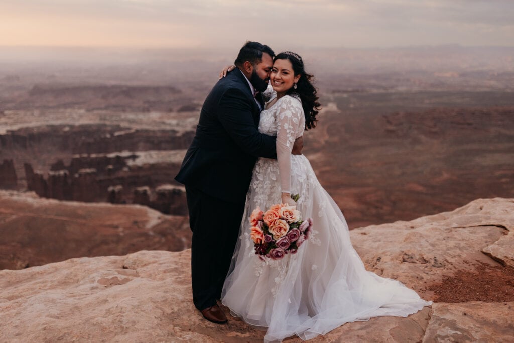 A bride smiles at the camera at sunrise after her first look with her groom.