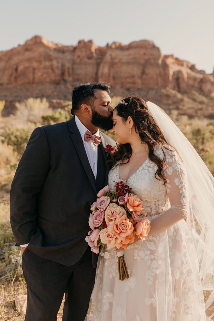 The groom kisses the bride on the forehead.