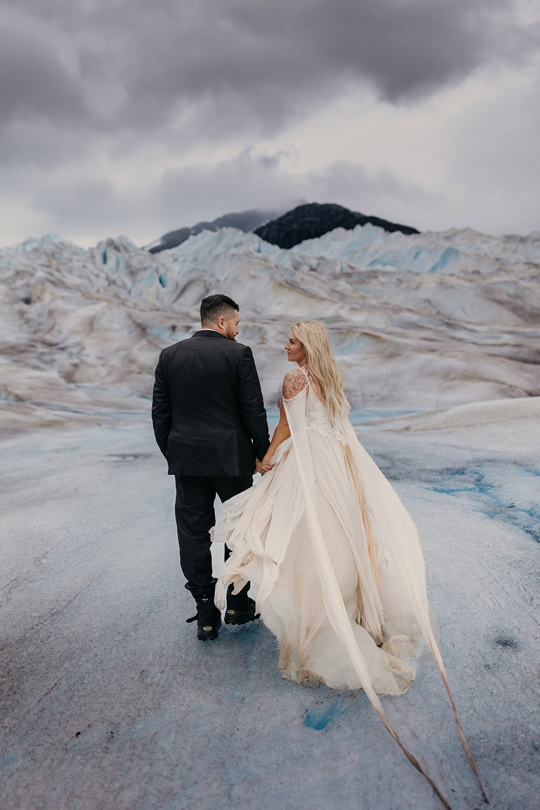 A couple holds hands and walks across Hubert glacier in Juneau, Alaska.