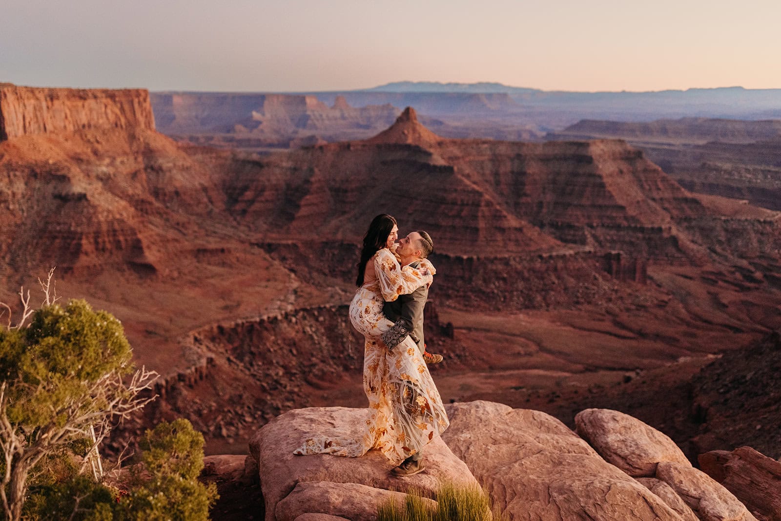 A groom picks up his bride on a fall evening after sunset standing on a sand stone cliff. 