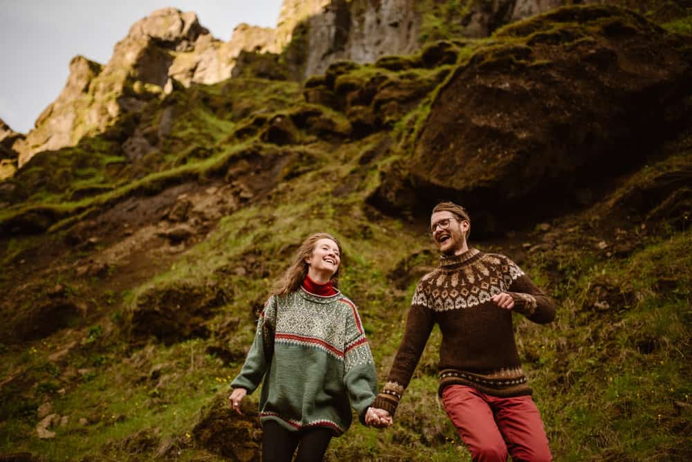 A couple holds hands and runs around a canyon in iceland giddy.