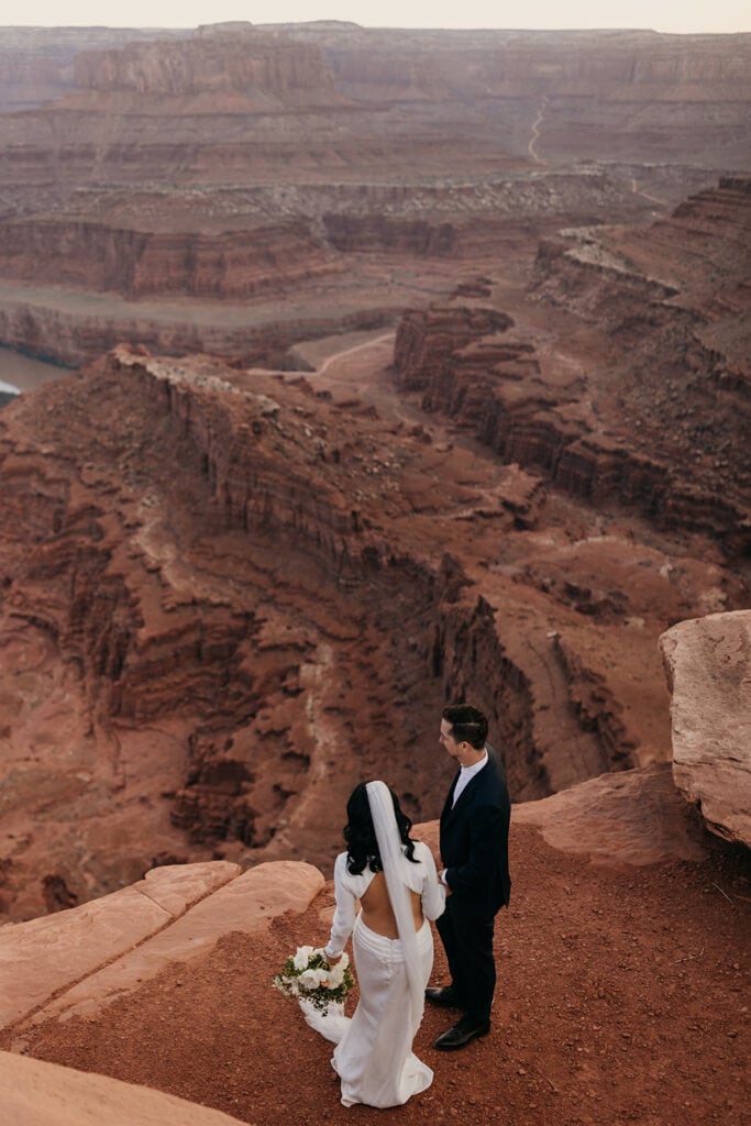 A bride and groom stand together at Dead Horse Point at Sunset