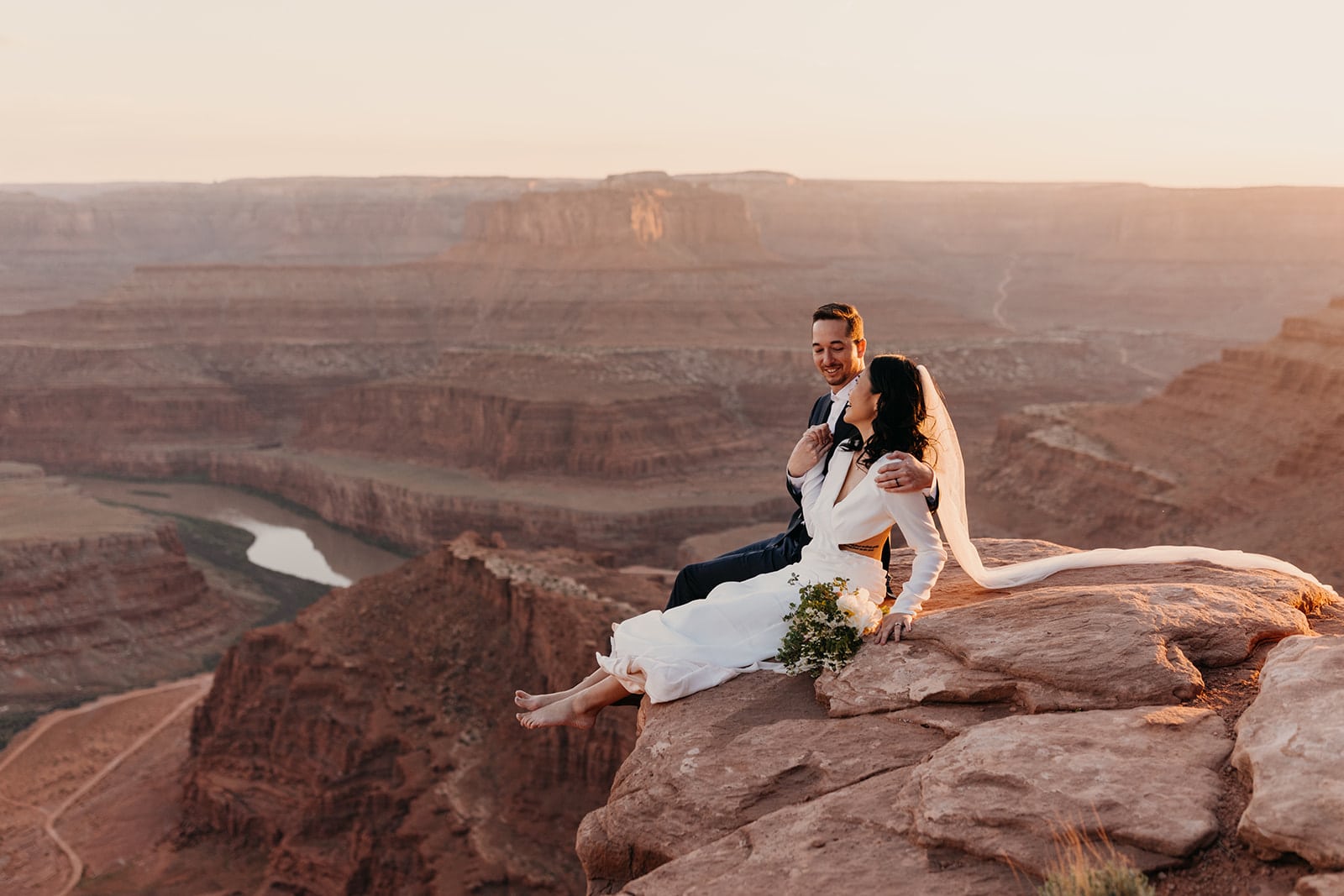 A bride and groom sit together at Dead Horse Point at Sunset