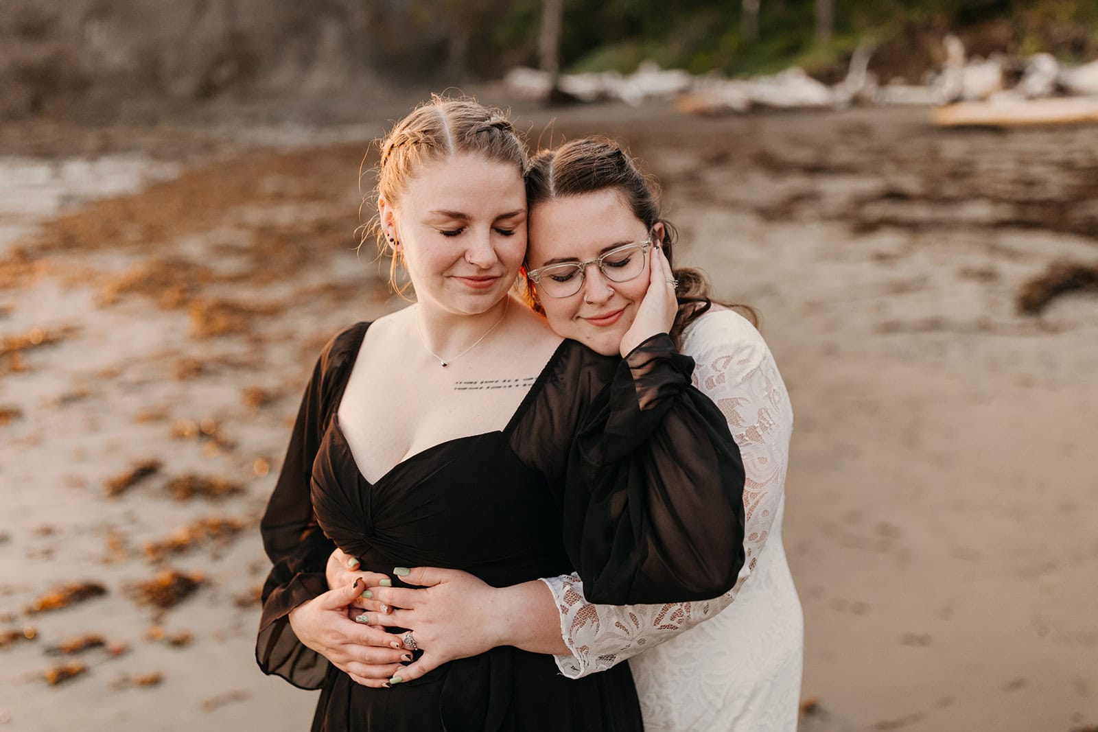 Two brides hold each other closely on the beach.