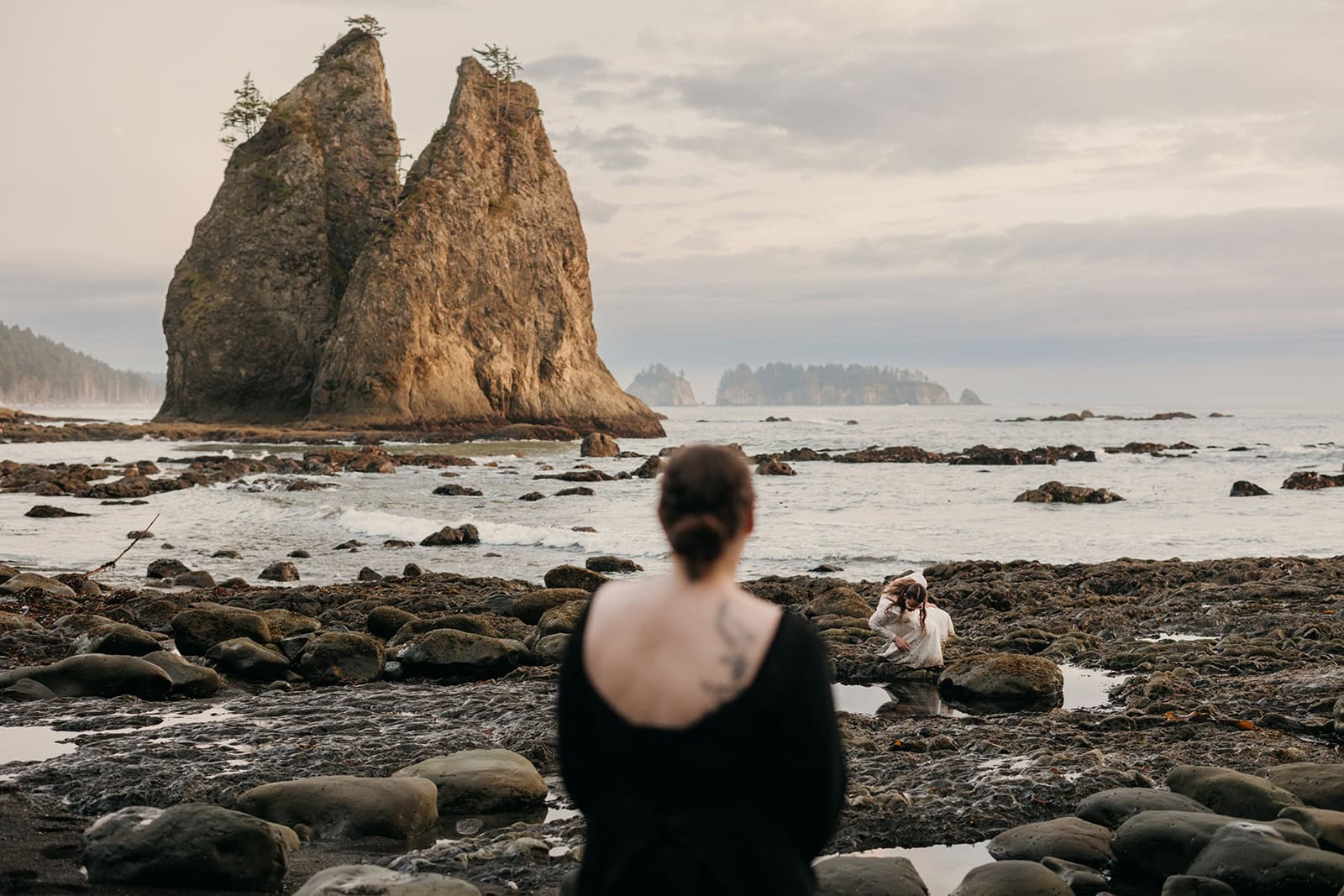 A bride watches her bride look at star fish along the Washington shoreline.