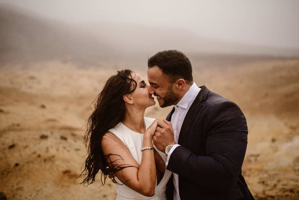 A groom smiles as he brings his bride in for a kiss on a rainy day in Iceland.