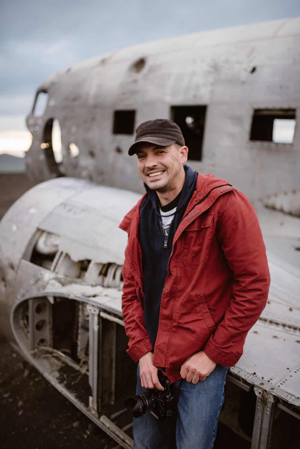 Portrait of a man in a red jacket sitting on a crashed plane.