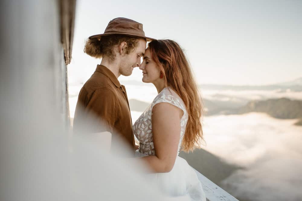 A couple stands together at high rock lookout. 